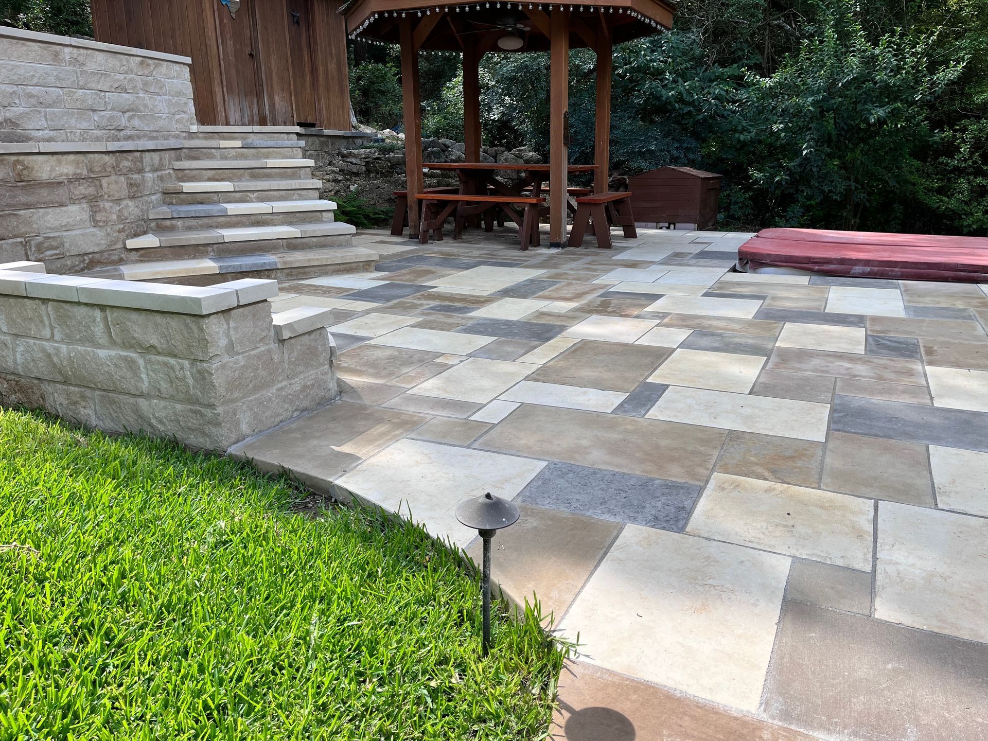 Stone patio with steps, wooden pergola, and lawn edging in a landscaped yard