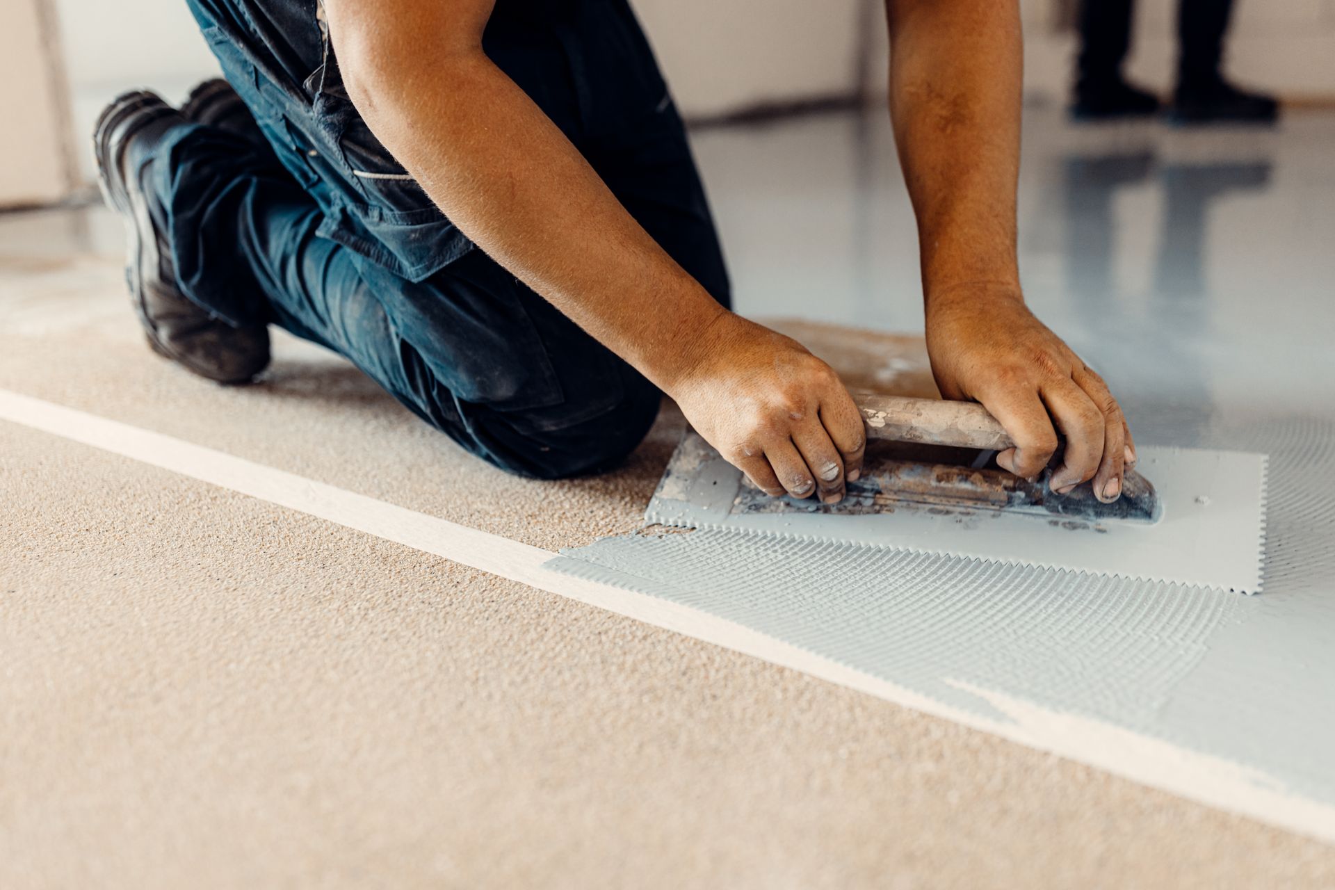 Person kneeling and smoothing wet floor coating with a trowel indoors