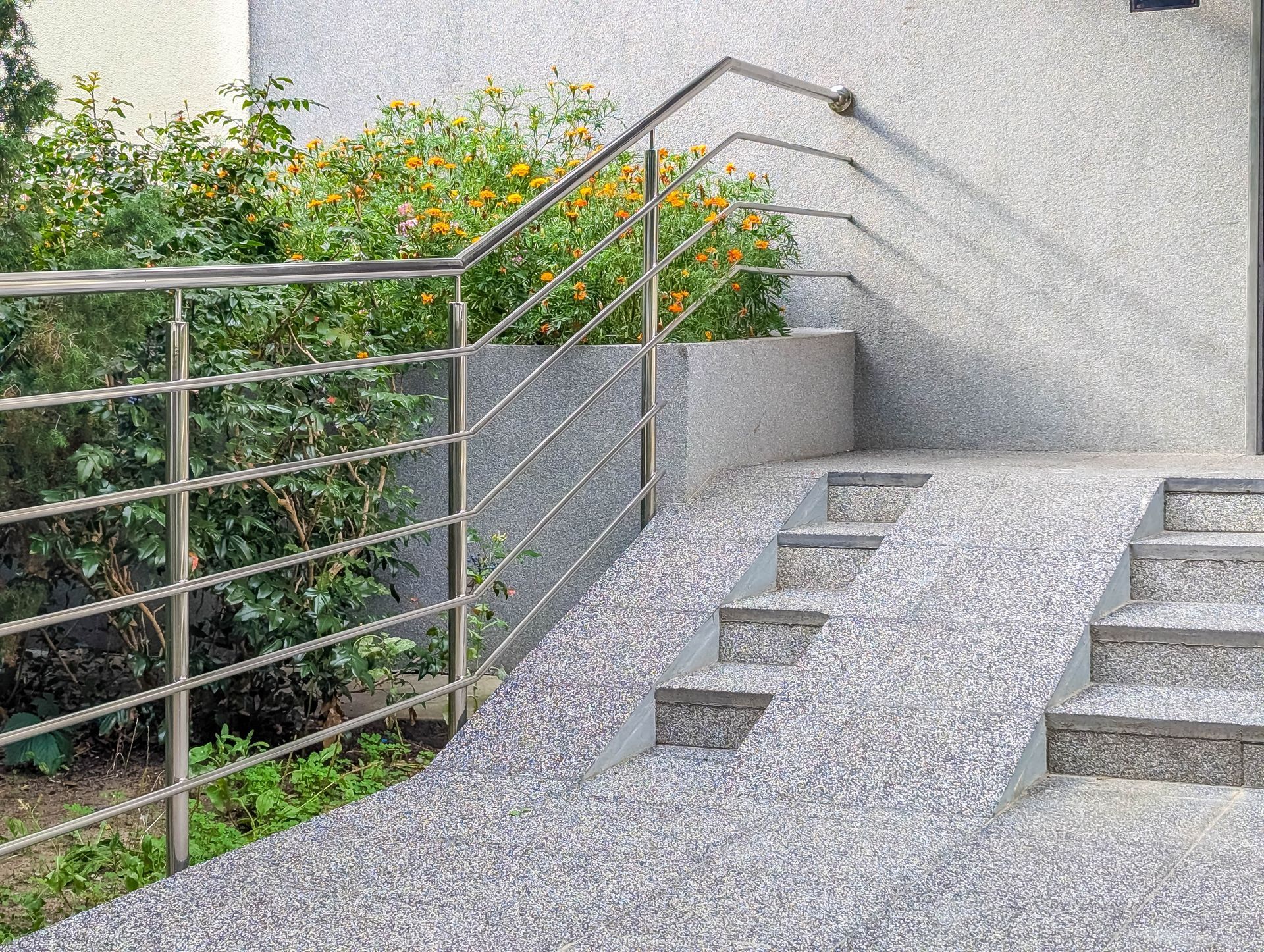 Concrete ramp and steps with stainless steel handrails beside a building and greenery