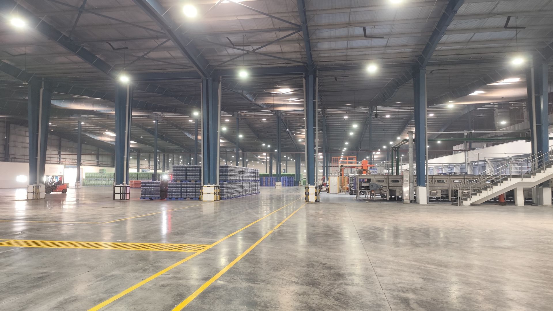 Empty warehouse interior with polished concrete floor, steel columns, and overhead lights.