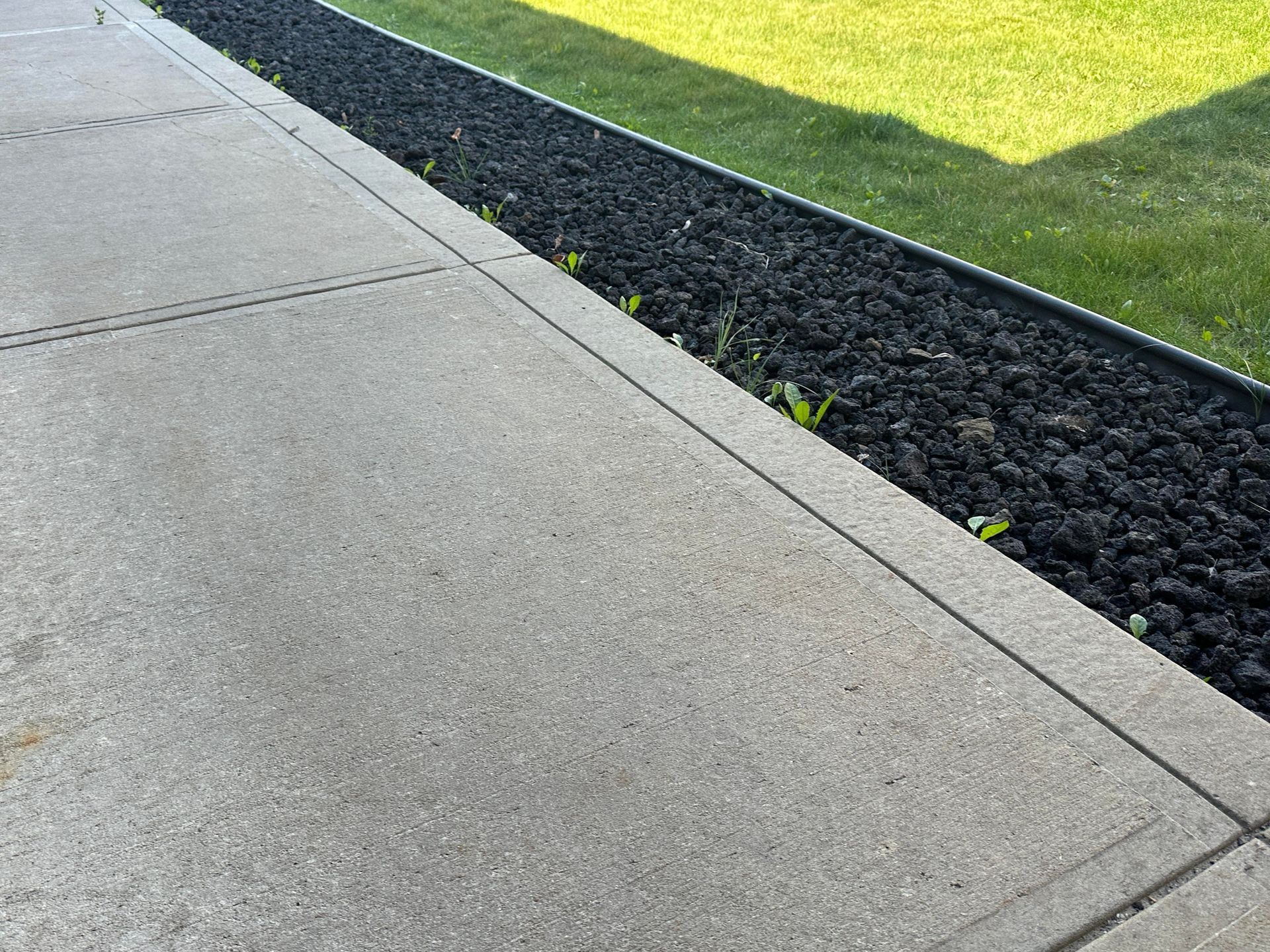 Concrete sidewalk beside a black mulch strip and green grass in sunlight