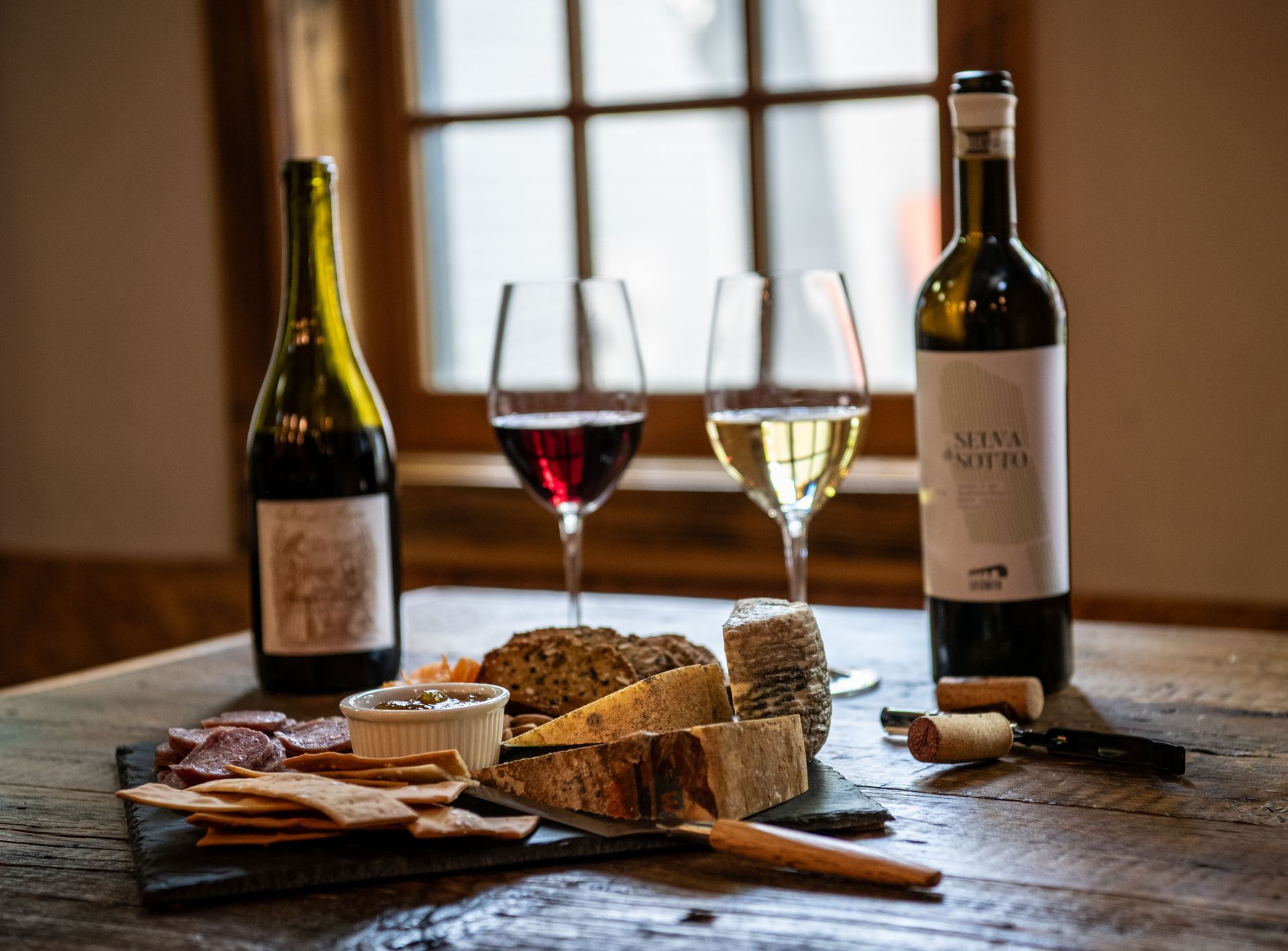 Two bottles of wine and two glasses of wine are on a wooden table available at Wine & Cheese Depot, Ludlow VT