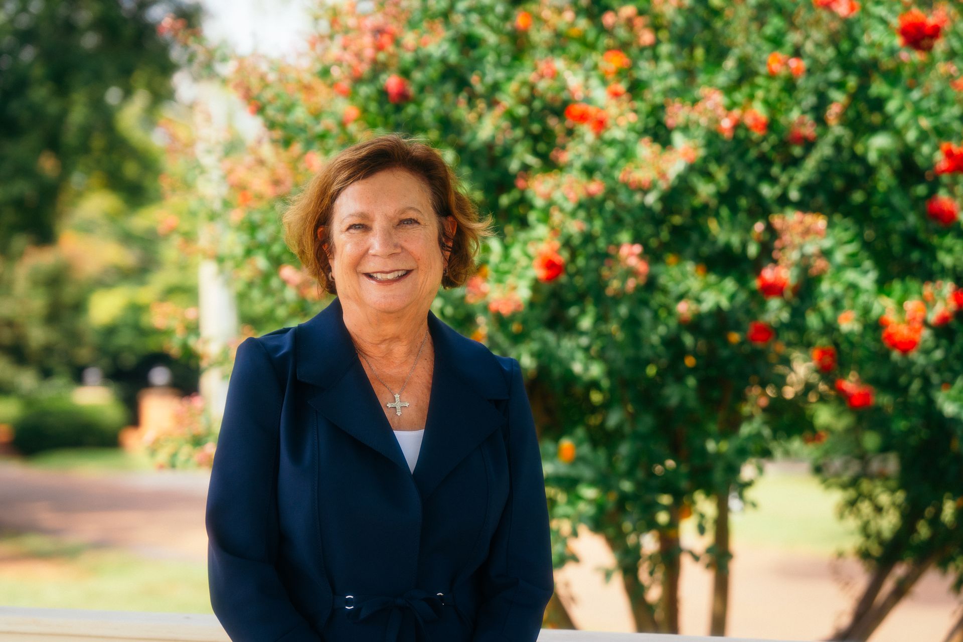 Woman in a navy blazer smiling outdoors beside a flowering tree.