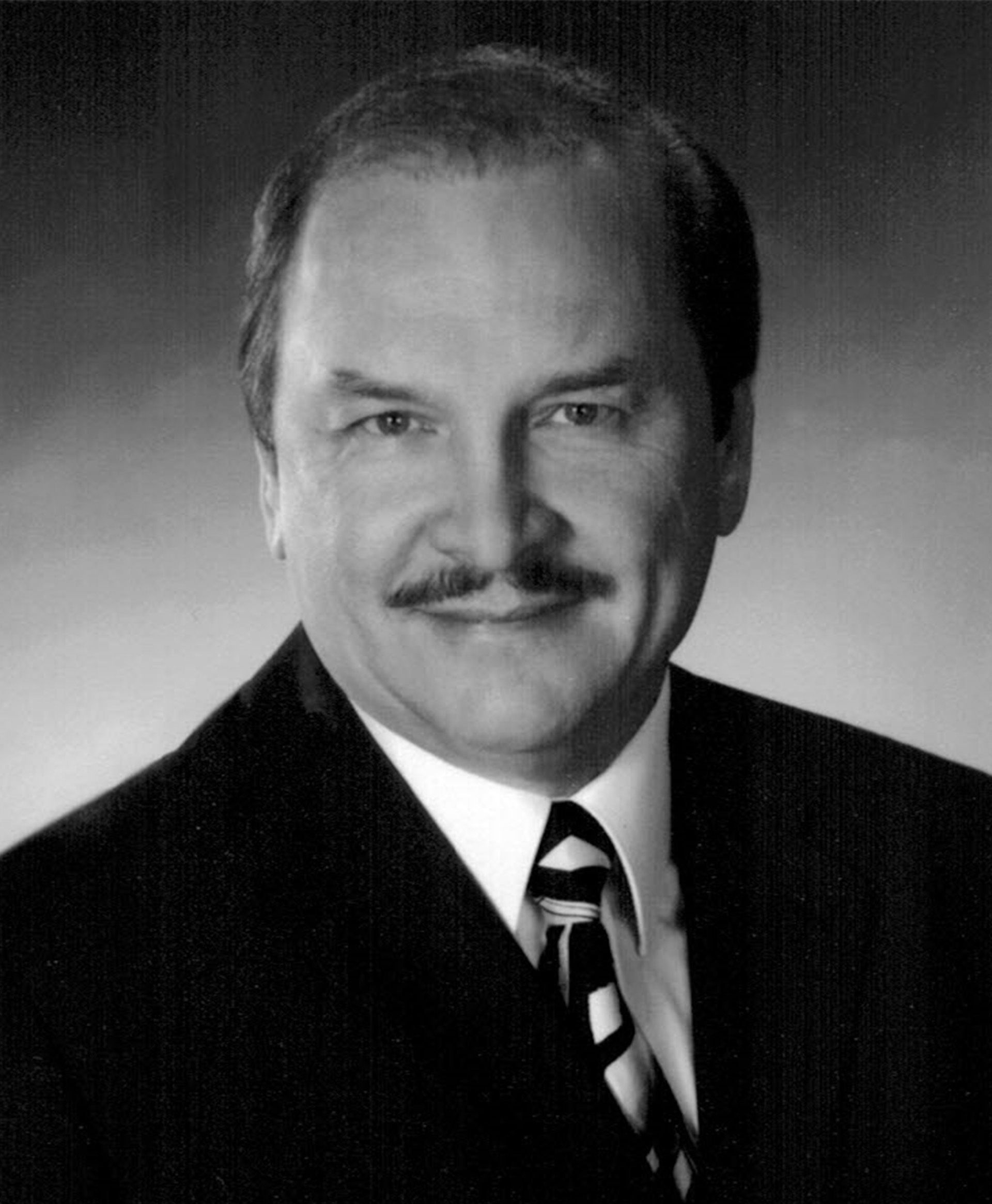 A man with a mustache is wearing a suit and tie.