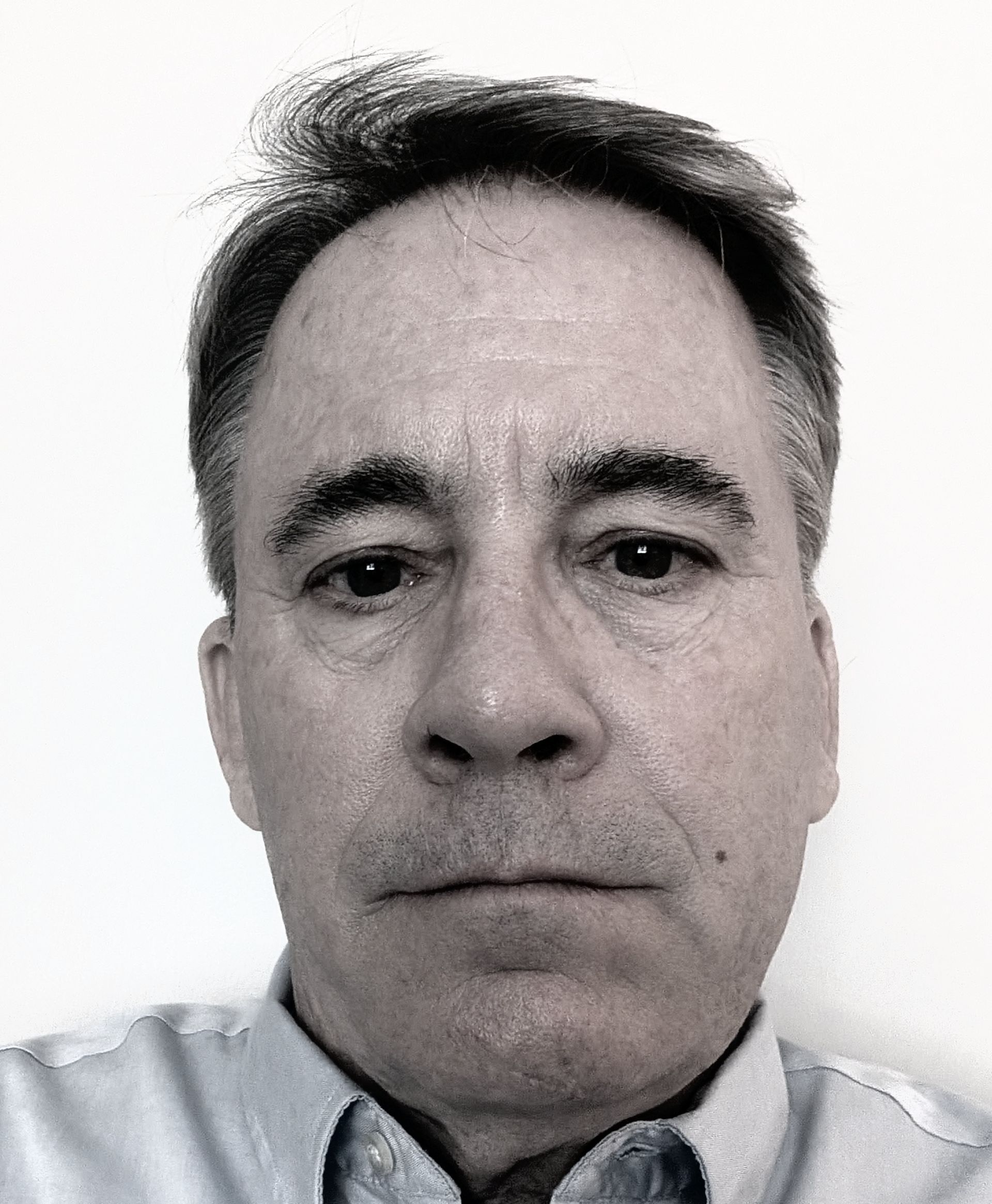A man in a blue shirt is looking at the camera in a black and white photo.