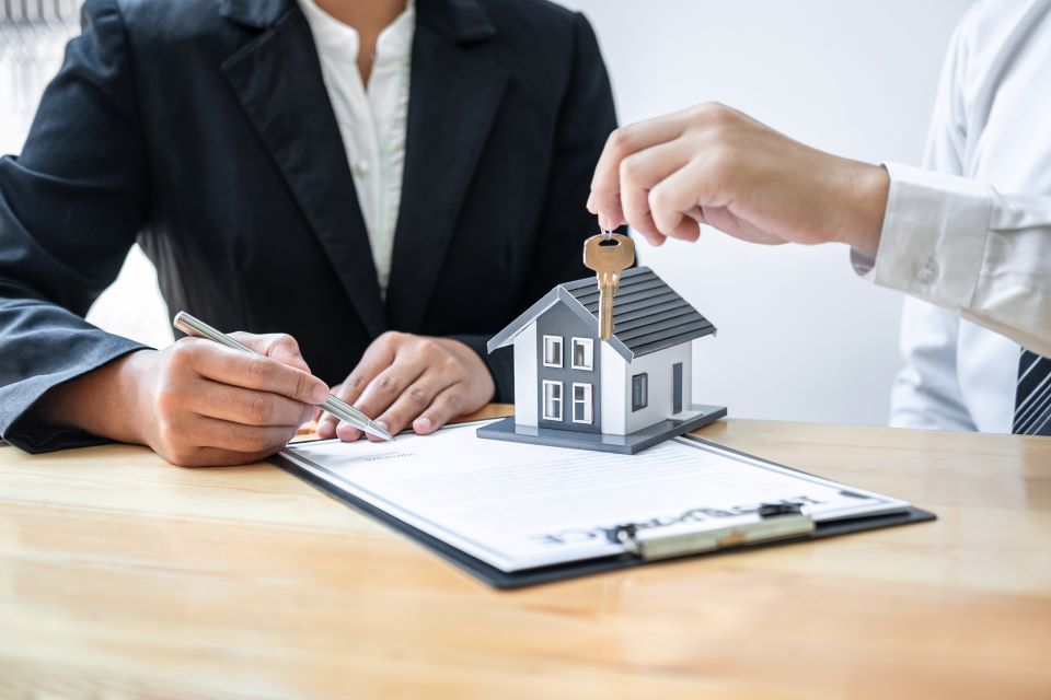 A man is giving a house key to a woman who is signing a contract.