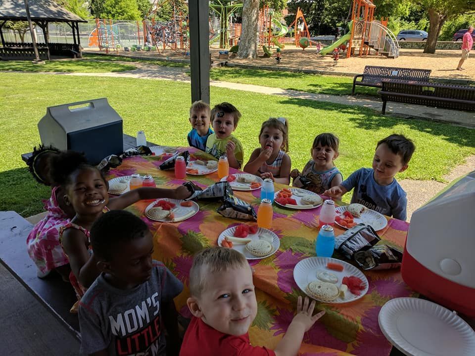 Children at a picnic table outdoors, smiling and eating watermelon.