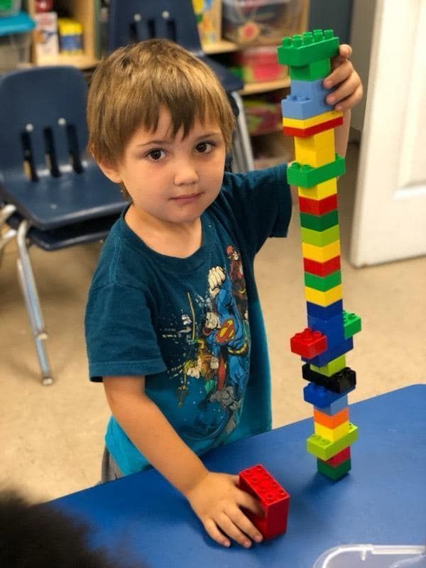Young boy with brown hair smiling, holding a tall tower of colorful blocks, in a classroom. Young boy with brown hair smiling, holding a tall tower of colorful blocks, in a classroom.