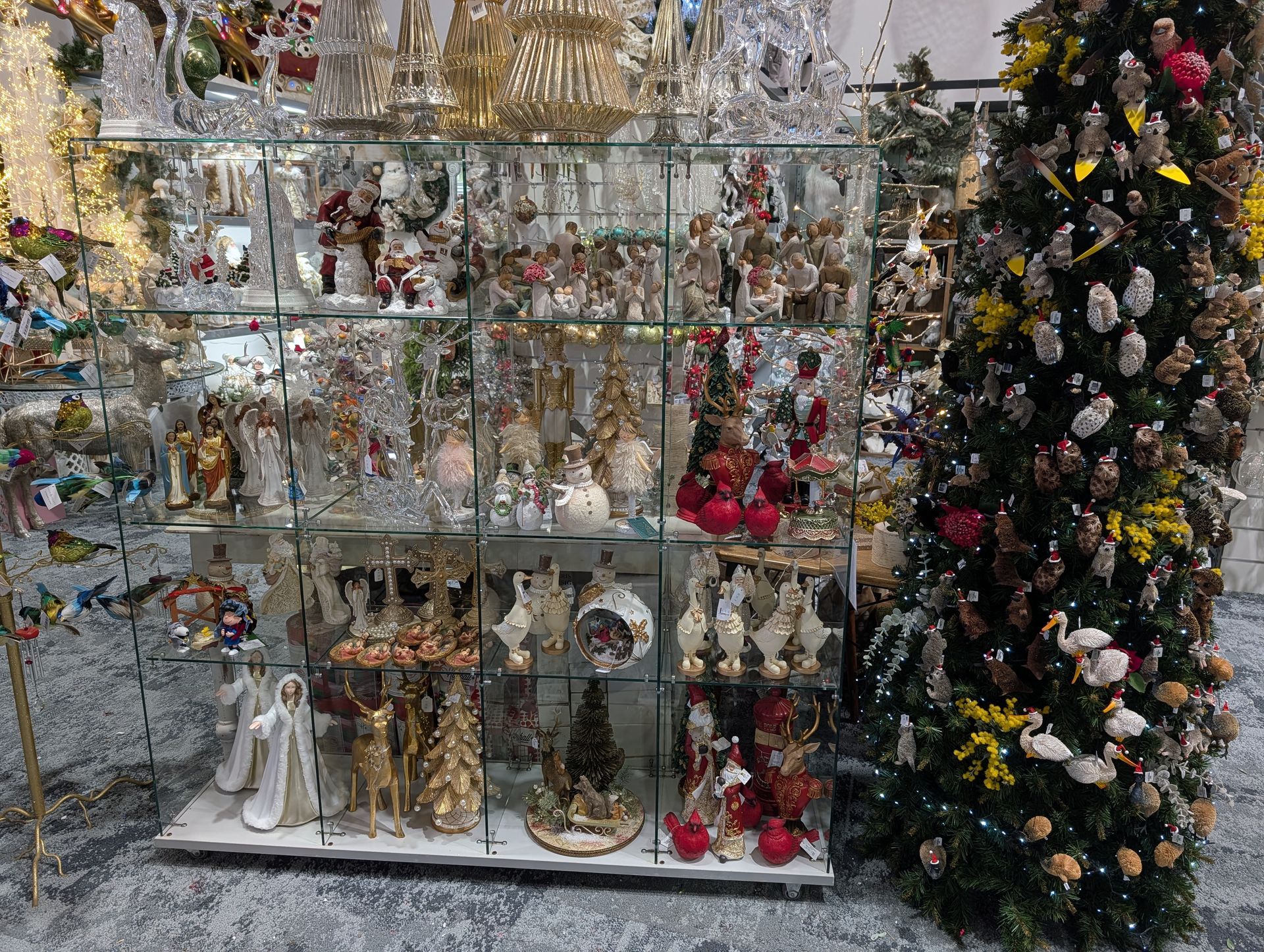 Shelves of glass ornaments and figurines beside a decorated Christmas tree in a shop display