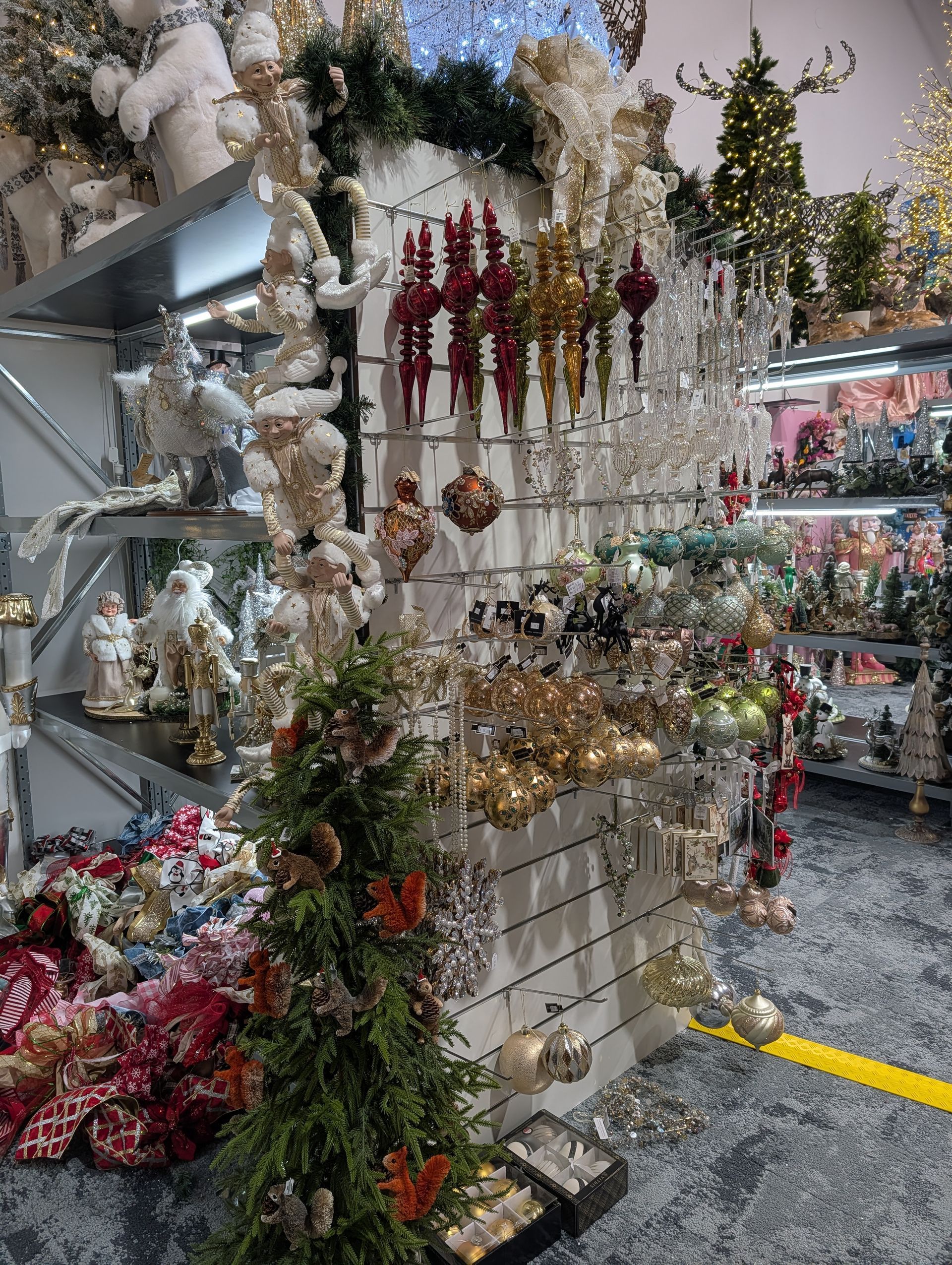 Christmas ornament display in a store aisle with garlands, red and gold decorations, and gift items