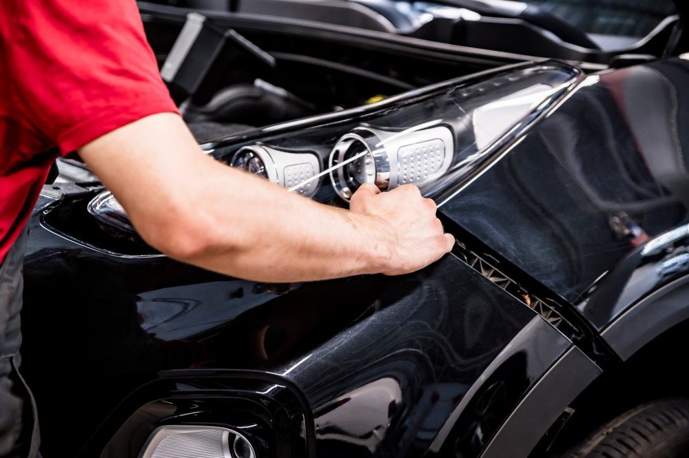 A Man in a Red Shirt is Working on a Black Car — Vanderpoel Smash Repairs in Bateau Bay, NSW
