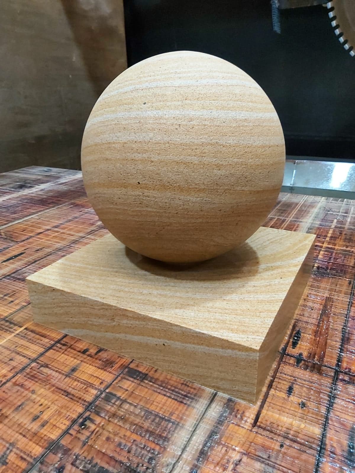 Beige textured sphere sculpture on a square wooden base atop a patterned table