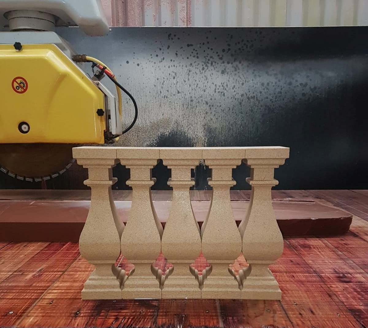 Woodworking machine carving a beige balustrade panel on a reddish wood surface