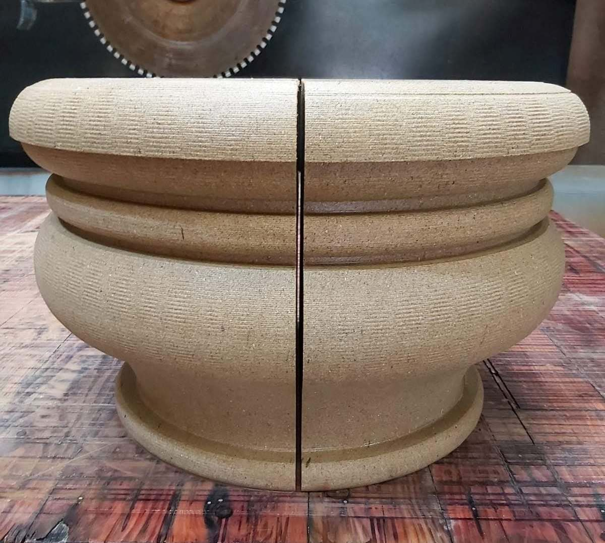 A beige wooden turned bowl or vase shape split down the middle on a worn workbench