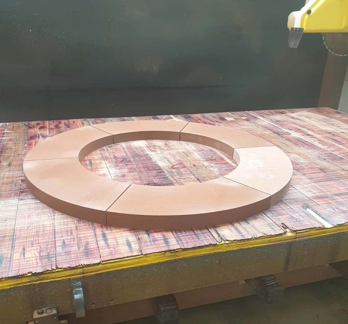 Brown ring-shaped wooden piece on a workbench in a workshop, with a machine arm at the top right
