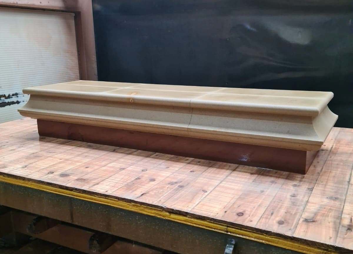 Long beige and brown wooden coffin or display case on a workbench in a workshop
