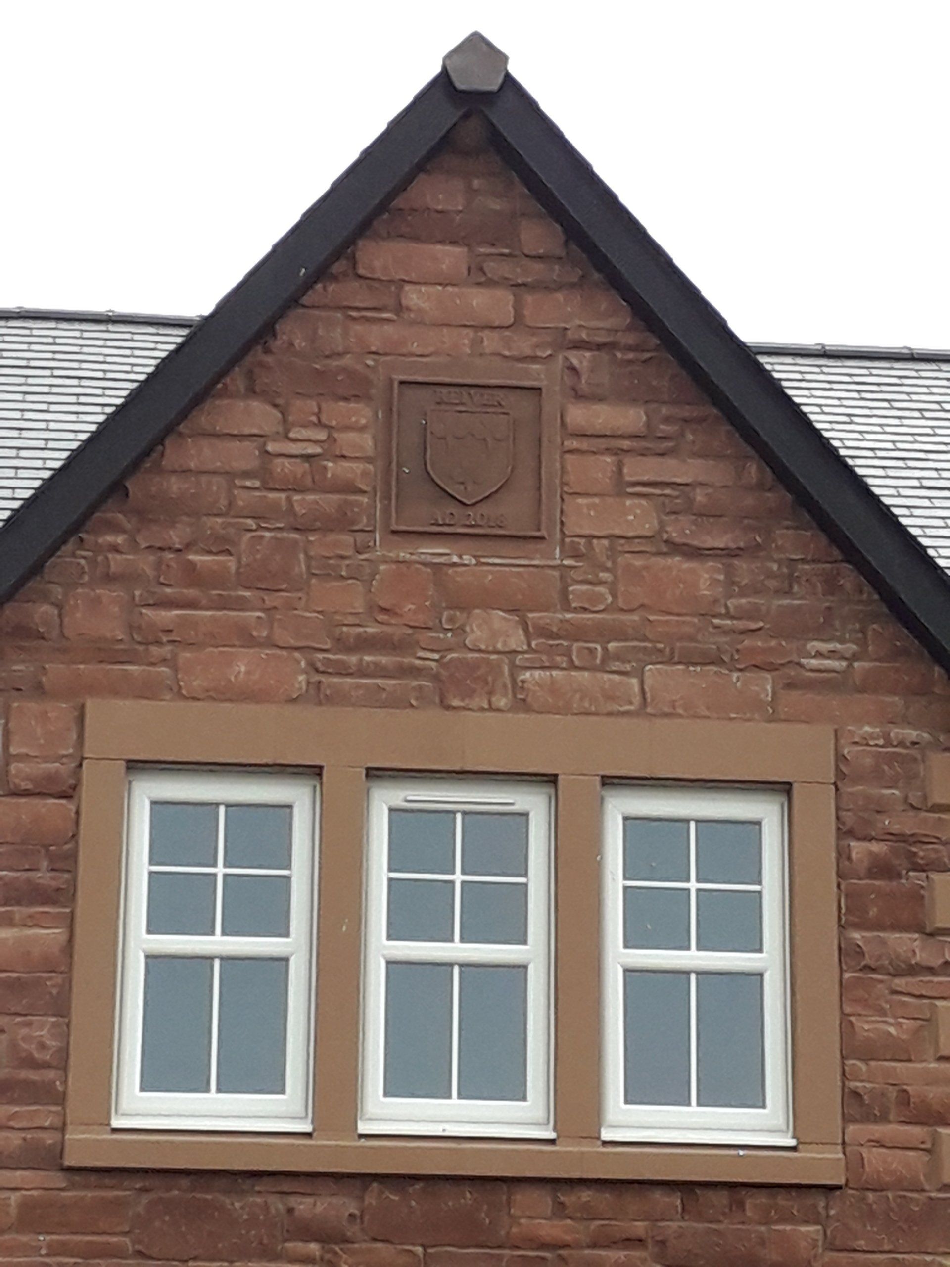 Brick house gable with three white-framed windows and a small decorative crest under dark roof trim