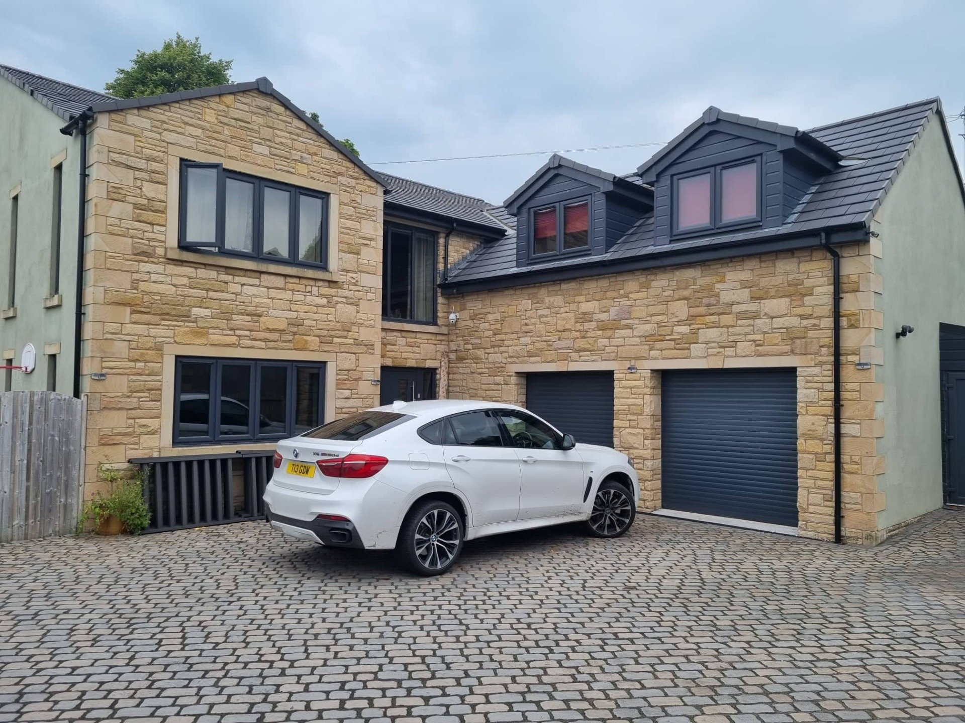 White sedan parked in front of a modern stone house with a garage and cobblestone driveway
