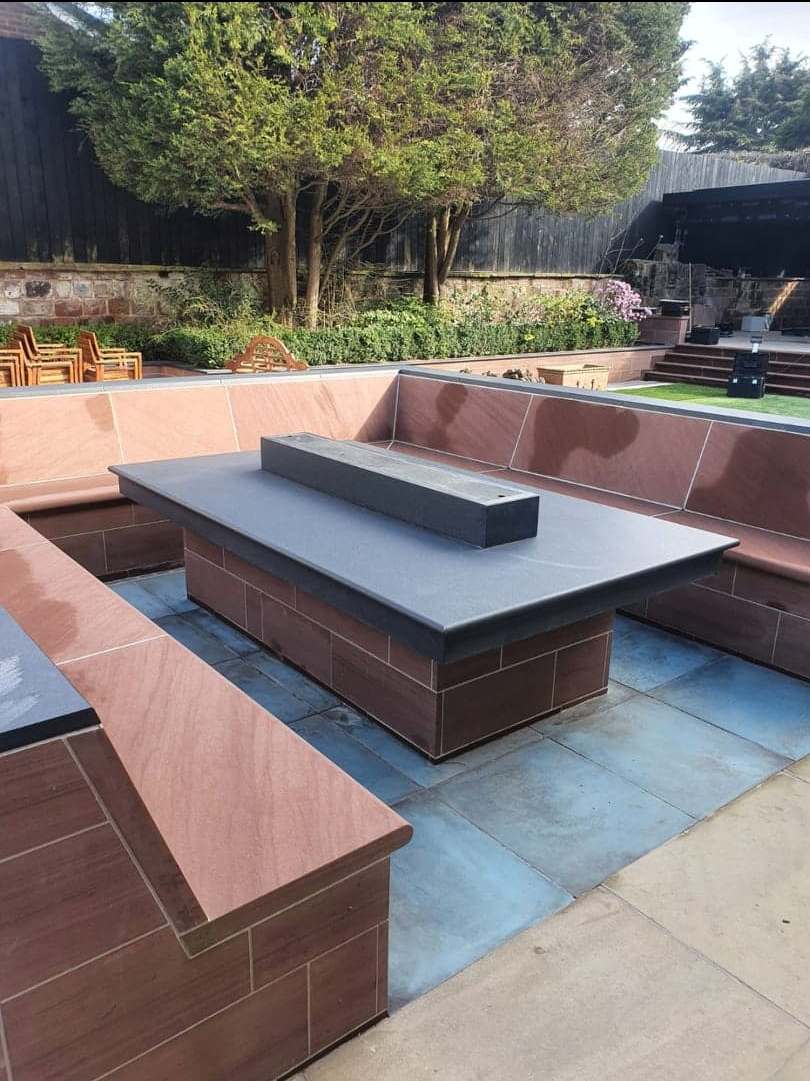 Outdoor patio with brown benches and a gray fire pit table in a landscaped garden