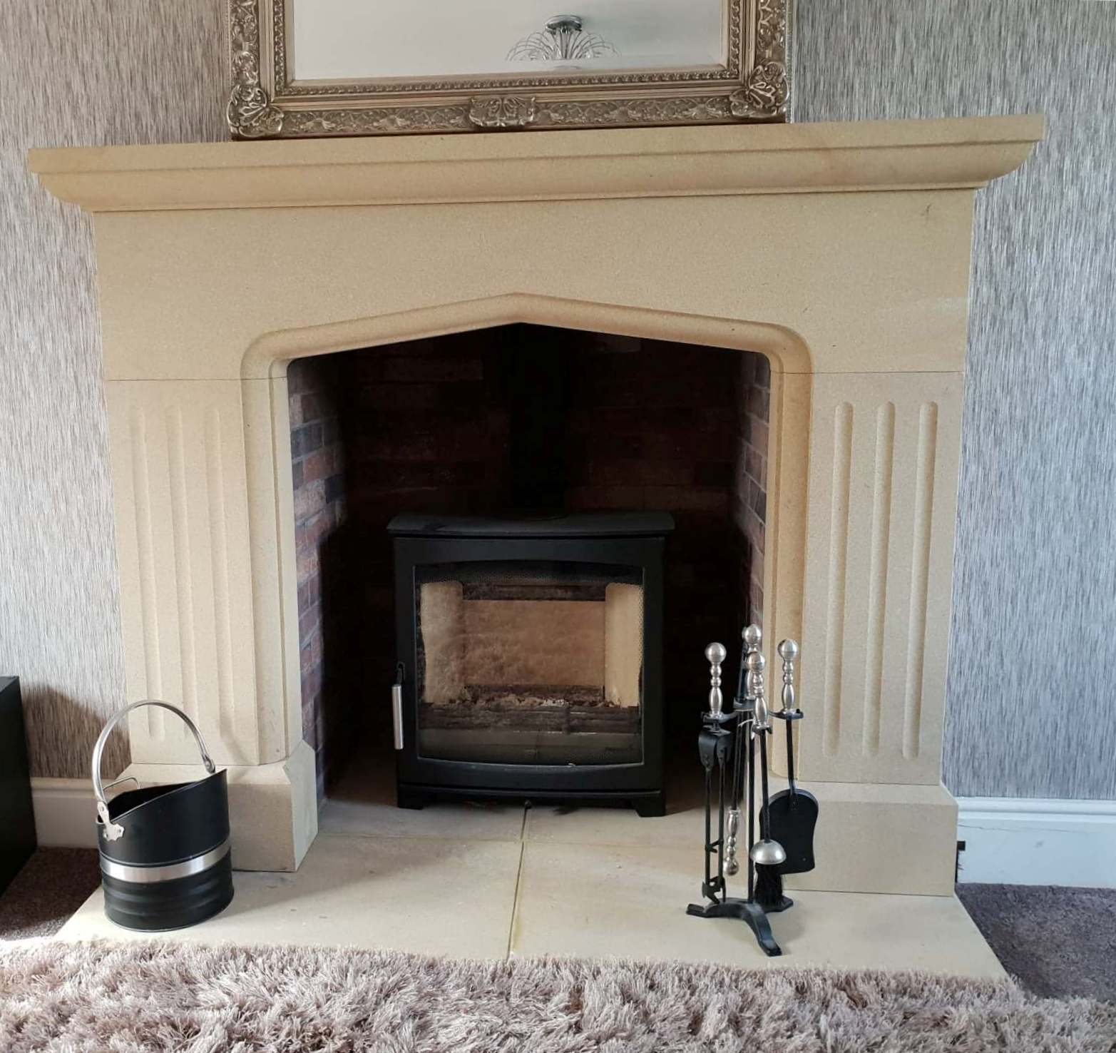 Cream fireplace with black fireguard, bucket, and log holder on a carpeted living room floor.