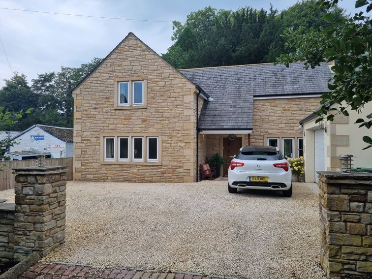 Stone house with gravel driveway and a white car parked in front