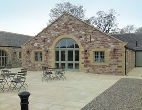 Stone courtyard with café tables outside a building with large arched windows and a gabled roof