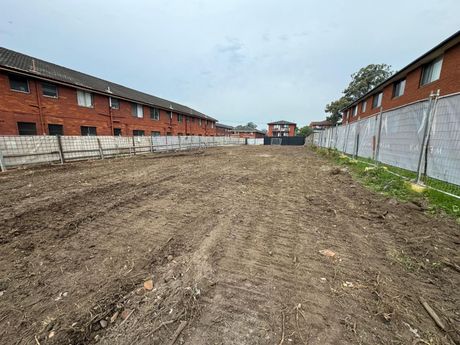 A dirt road leading to a brick building with a fence in the background.