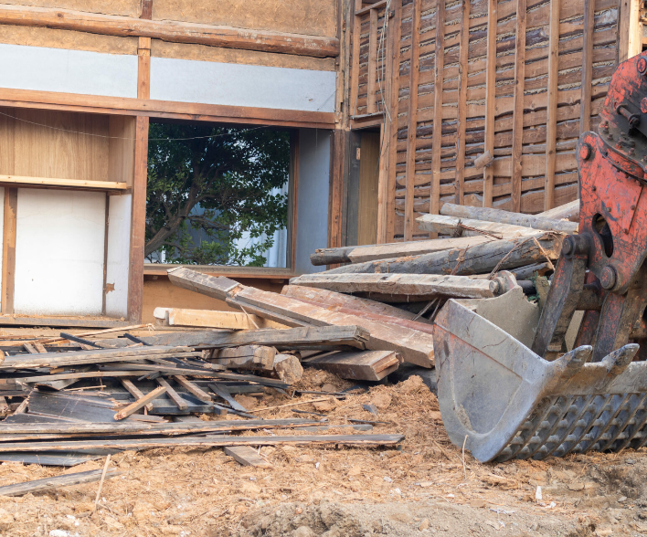 A bulldozer is demolishing a building with a pile of wood in front of it.