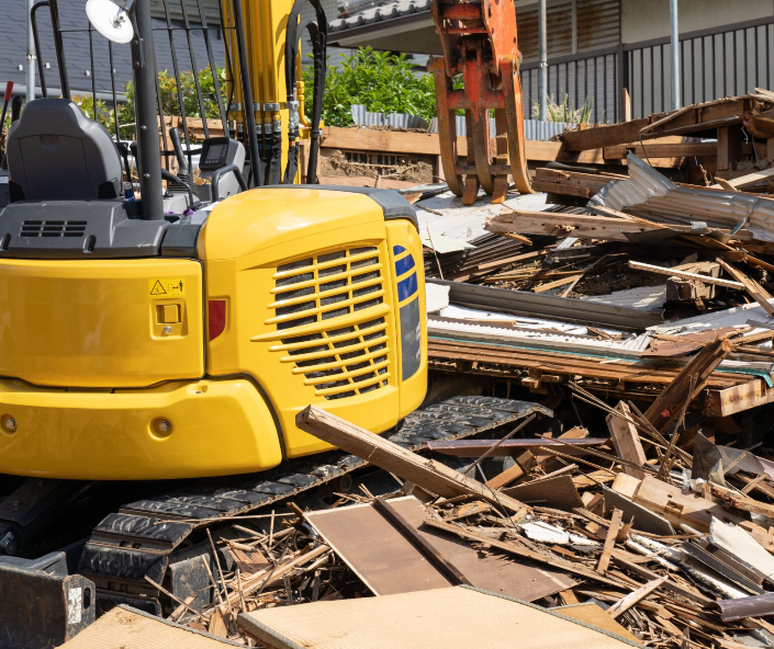 A yellow excavator is sitting on top of a pile of rubble.
