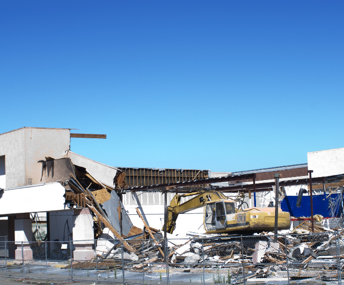 A large yellow excavator is demolishing a building