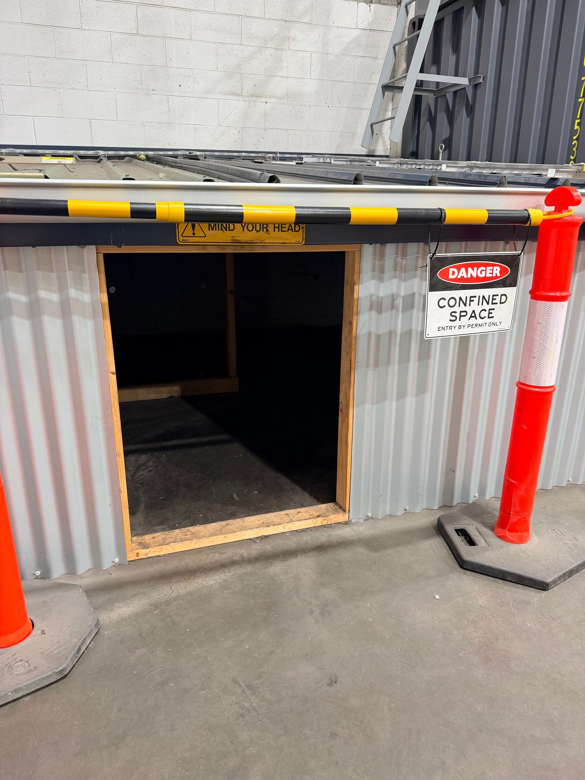 Photograph of a confined space entry point used for training marked by a rectangular opening in a corrugated metal wall