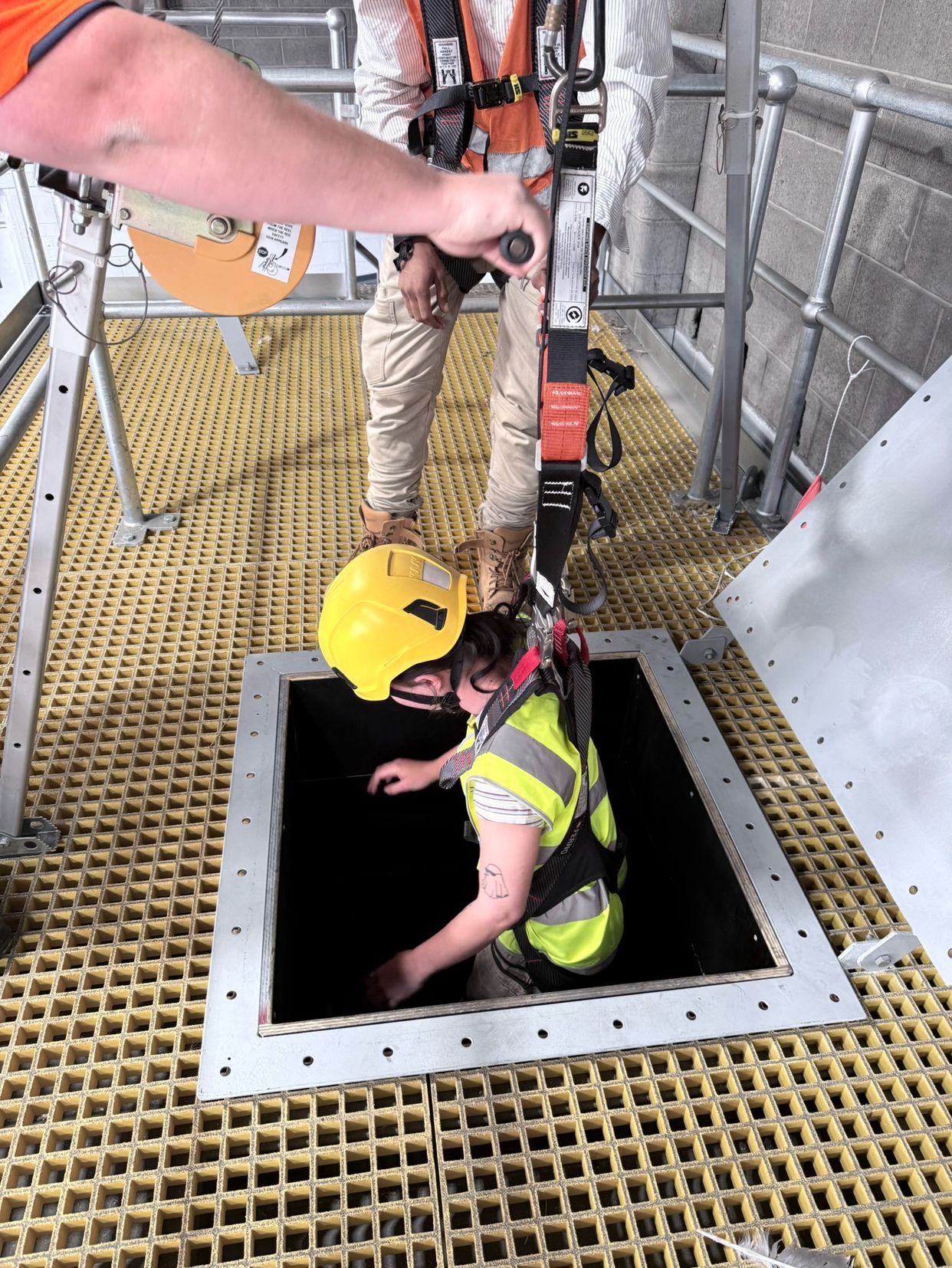 Confined space entry training scenario with a worker wearing a yellow safety helmet and high-visibility vest.