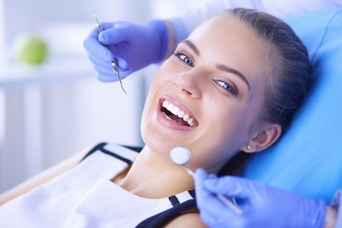 Smiling patient at the dentist as gloved hands use dental tools in a bright clinic.