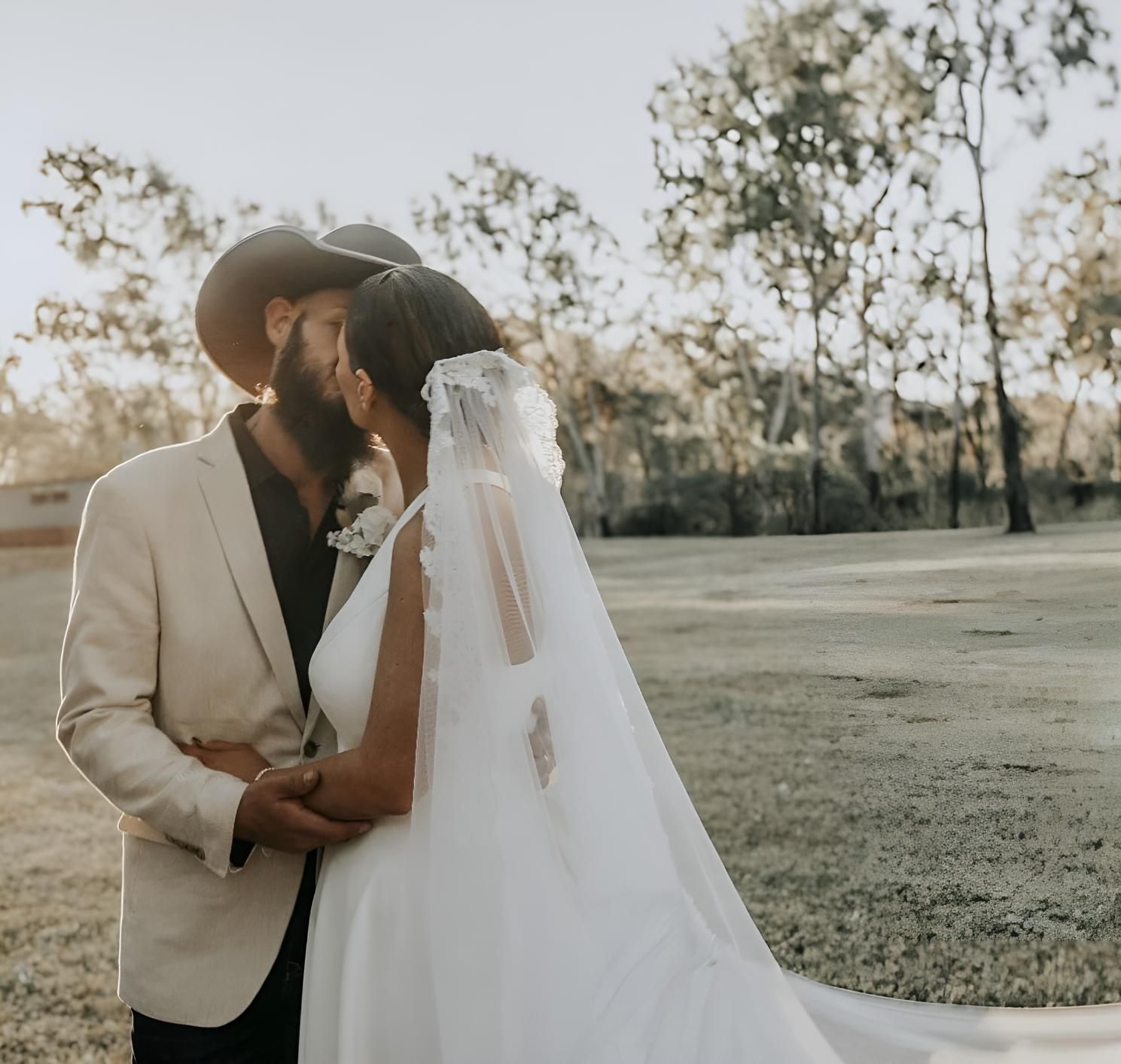 A Bride And Groom Kissing In A Field — Beautique Hair Lounge & Beauty Bar In Condon, QLD