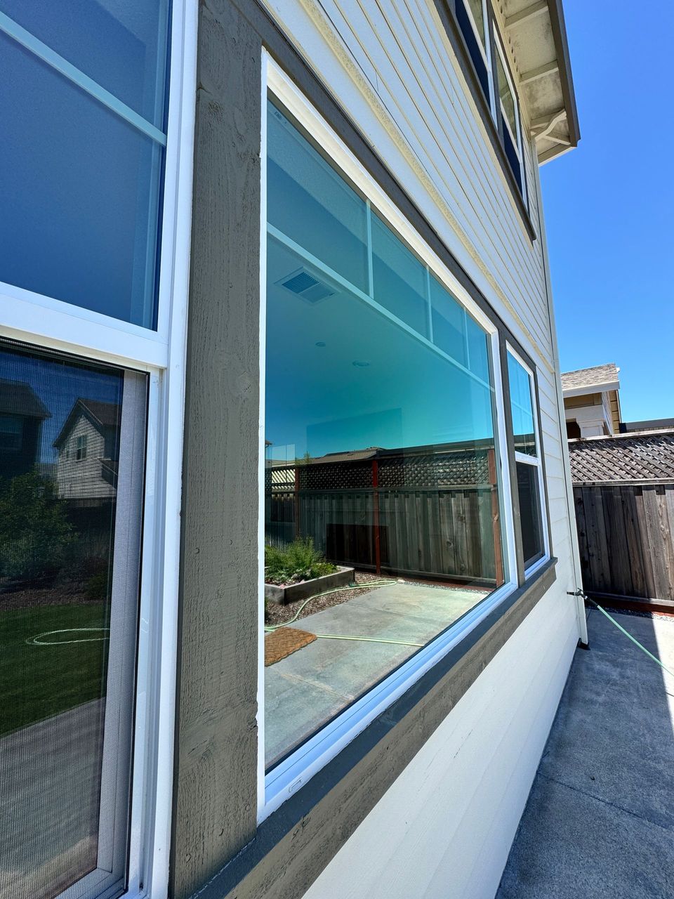 Exterior view of house windows reflecting a patio and neighboring homes, with blue sky visible