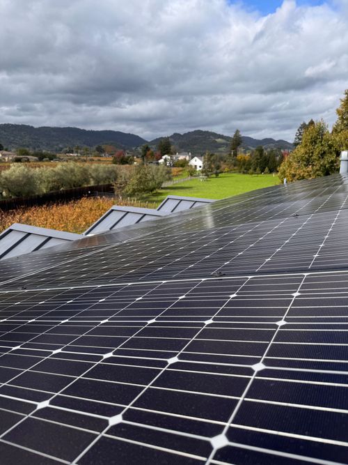 Solar panels on a rooftop under cloudy skies, with green hills in the background.