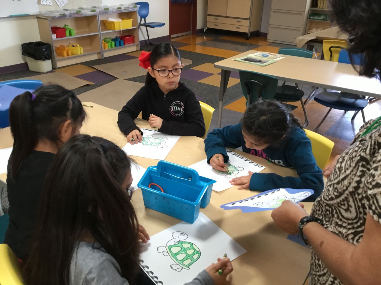A group of children are sitting around a table drawing a picture of a turtle