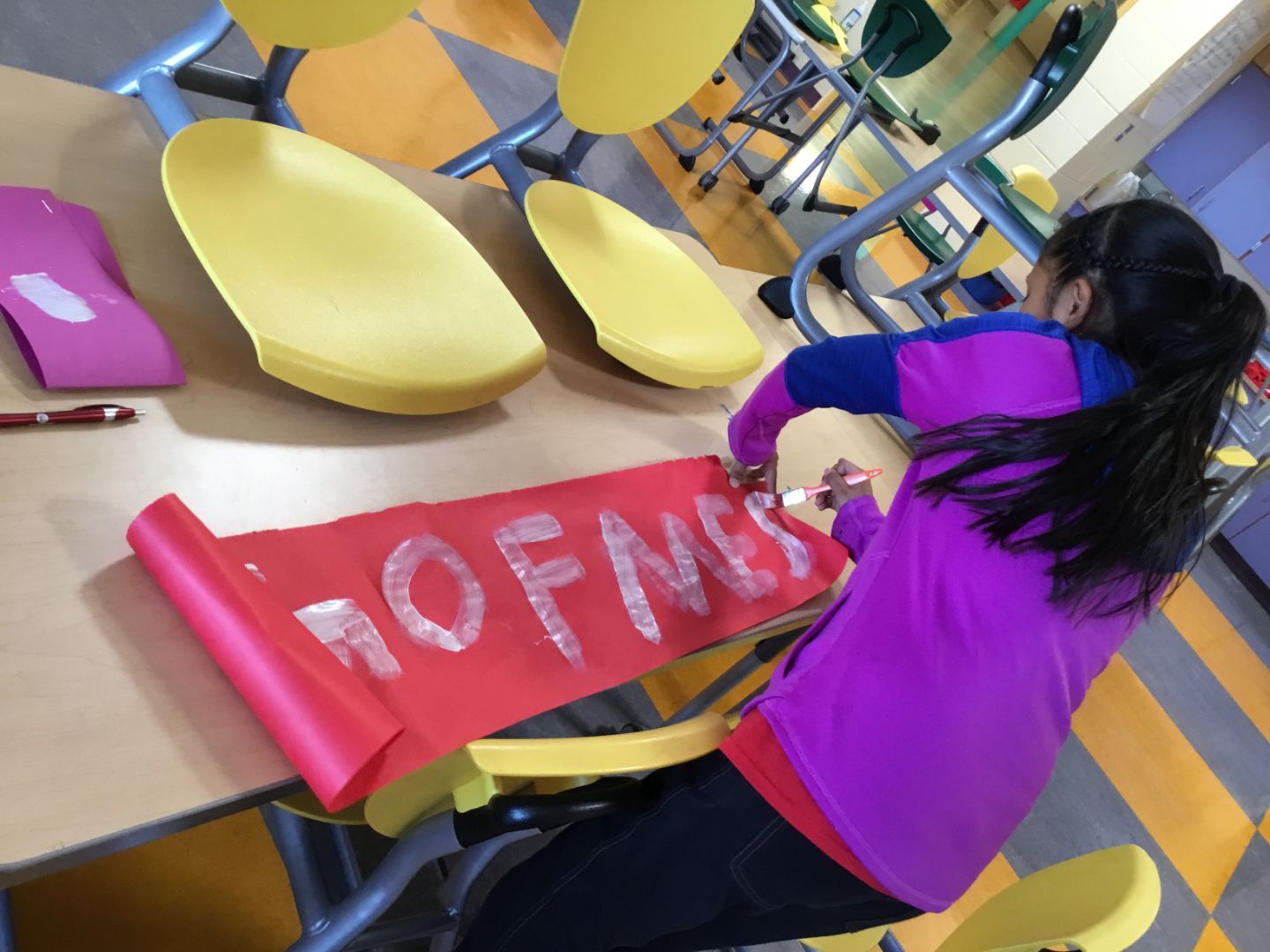 A girl sits at a table with a red piece of paper that says no fms