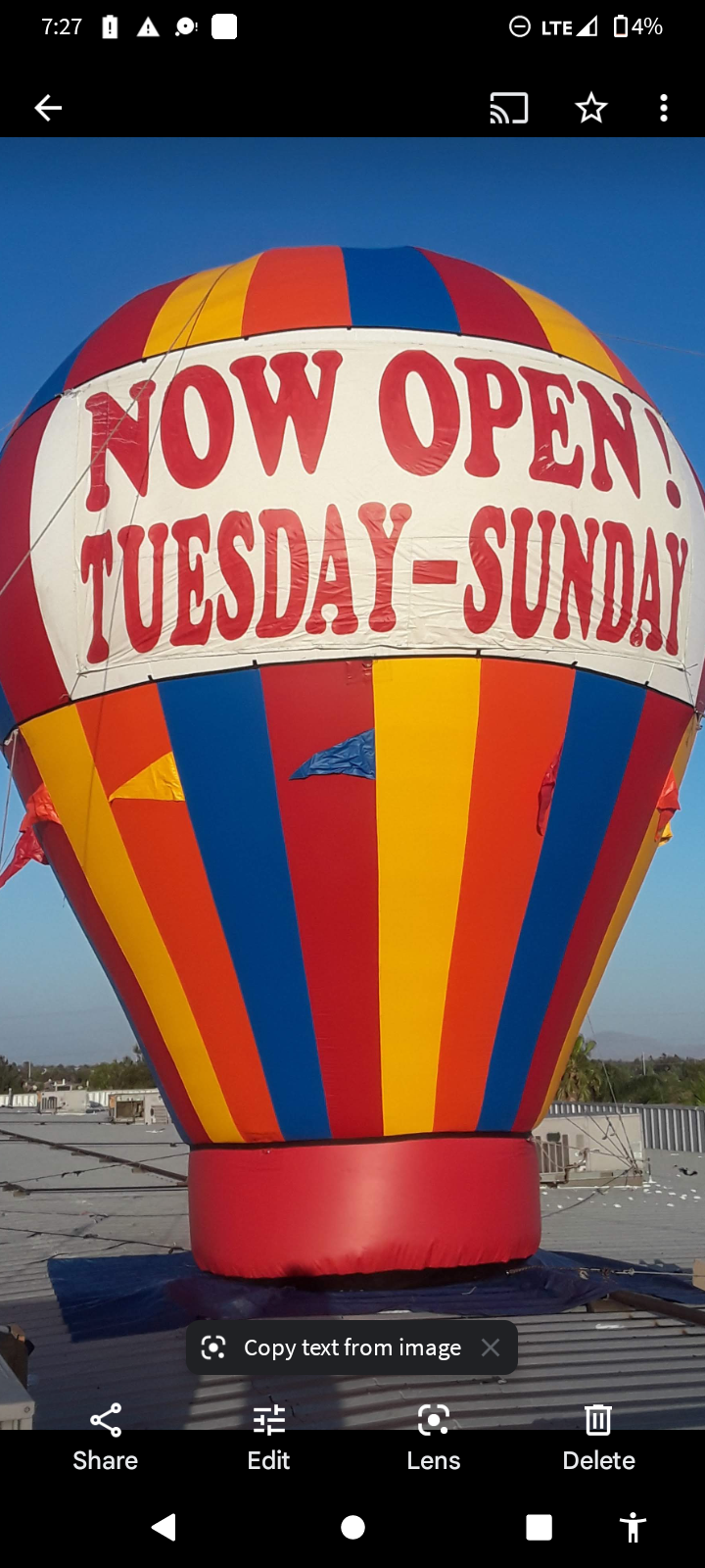 A colorful hot air balloon with a sign that says `` now open tuesday - sunday ''.