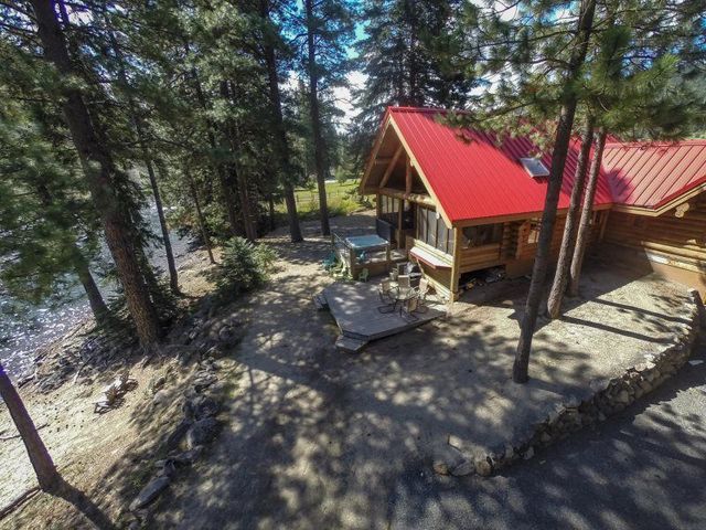 Wooden cabin with red roof in a forest clearing, with a deck and picnic table in dappled sunlight