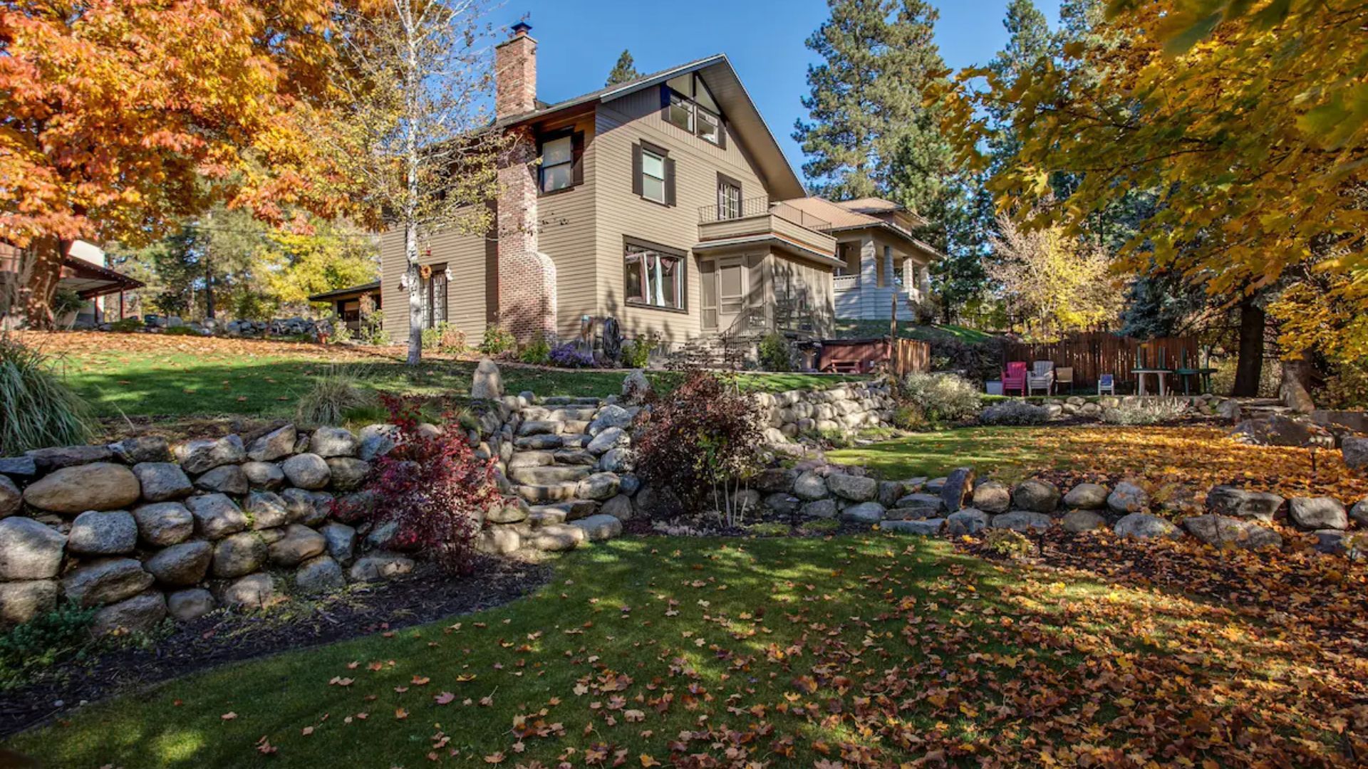 Stone house with autumn trees, stone retaining wall, and fallen leaves in a landscaped yard