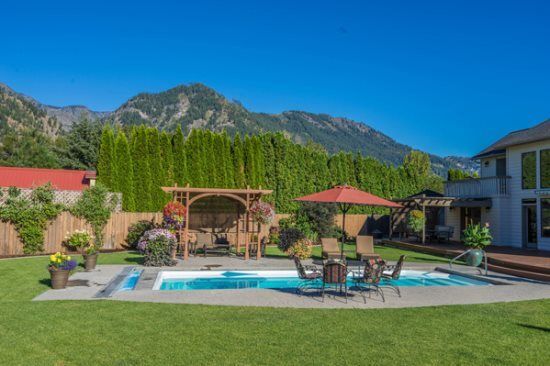 Backyard pool with patio furniture, pergola, and mountain view under a clear blue sky