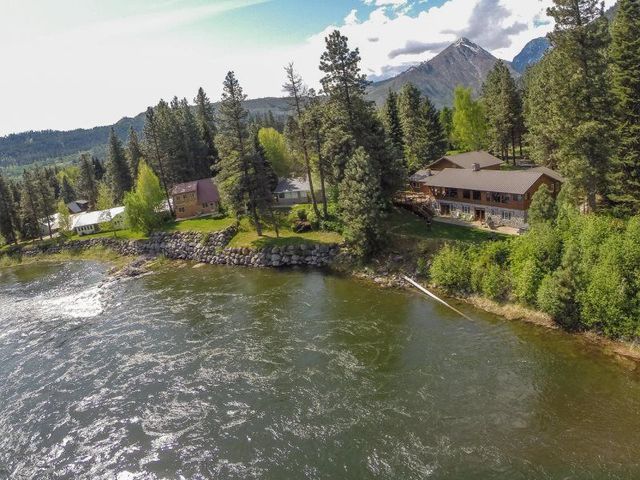 Riverside cabins among pine trees with a mountain backdrop and sunlit water in the foreground