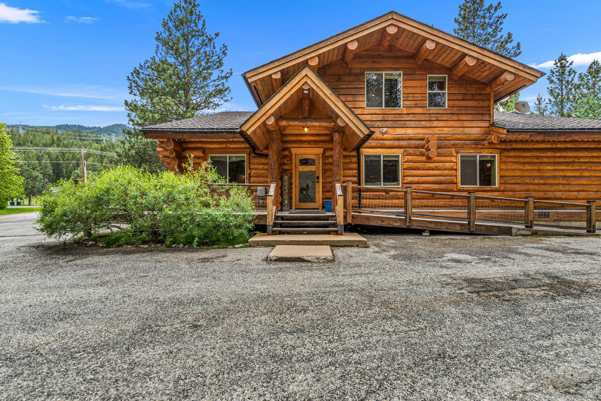 Log cabin home with log siding, gravel driveway, and trees in a rural setting