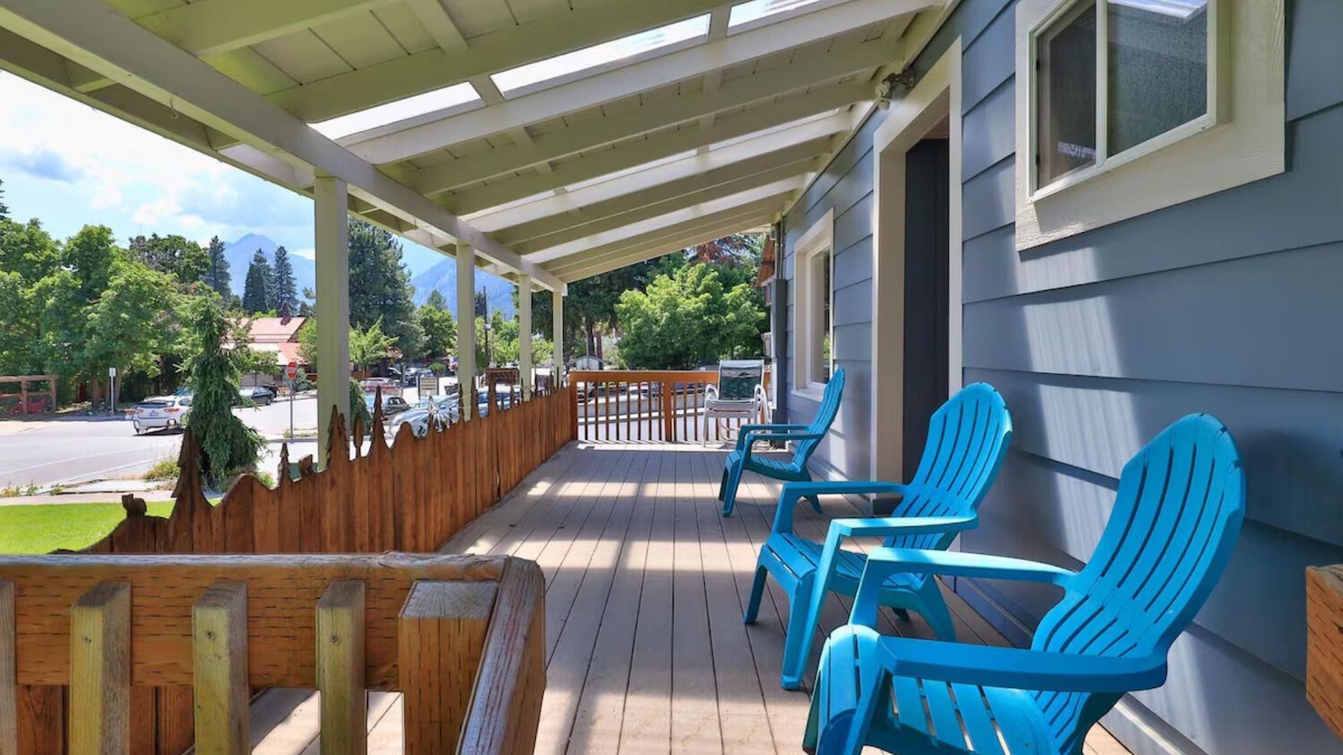Covered wooden porch with blue chairs, railing, and a view of the street and trees