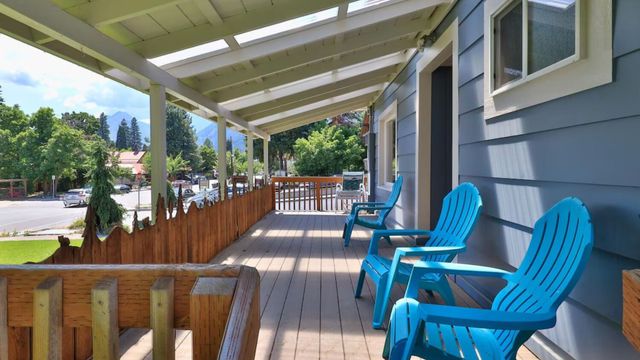Covered front porch with blue chairs, wooden railing, and a view of houses and trees.