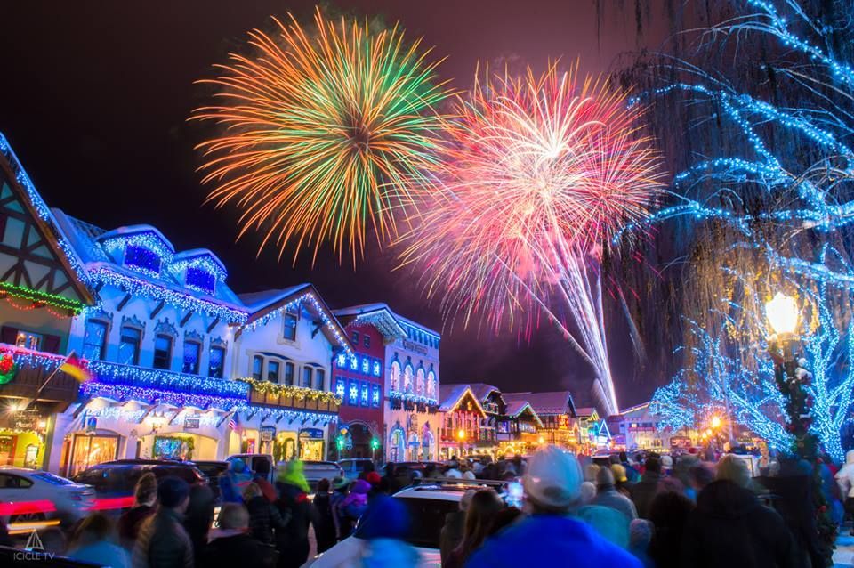 Crowded snowy street with lit shops and colorful fireworks overhead at night