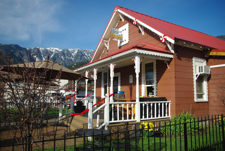Small red house with white trim and porch, black fence, and mountains in the background.