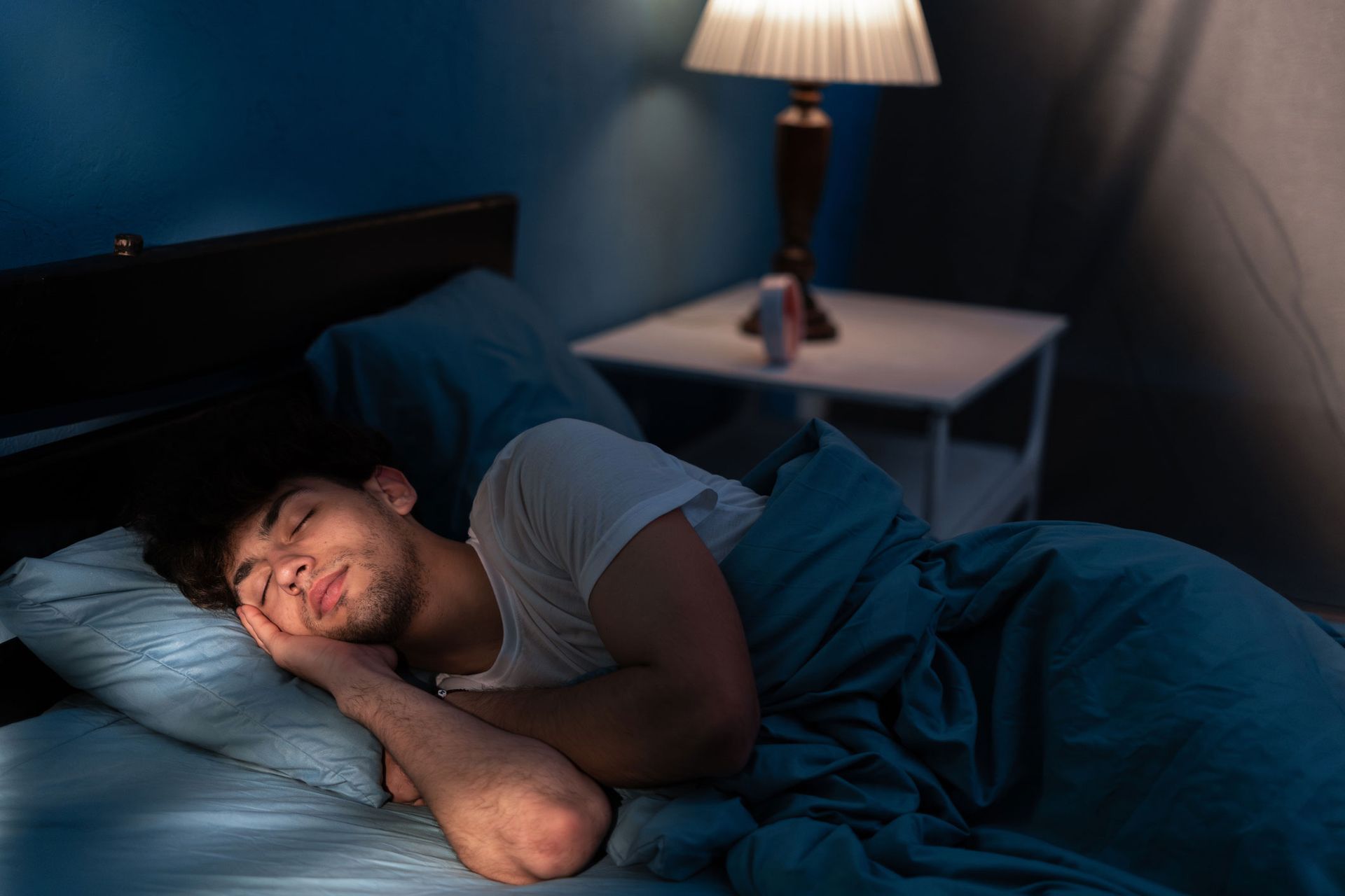 A man is sleeping in a bed with a lamp in the background. A man is sleeping in a bed with a lamp in the background.