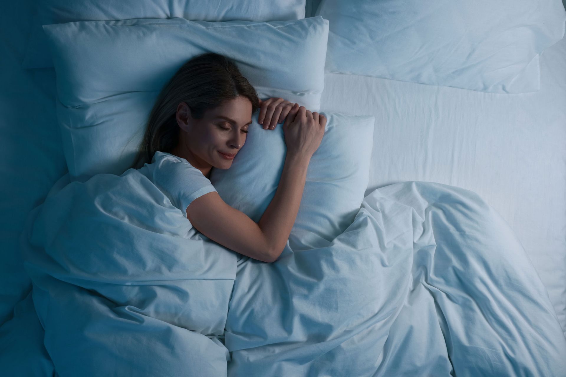 A woman is sleeping in a bed with white sheets and pillows. A woman is sleeping in a bed with white sheets and pillows.